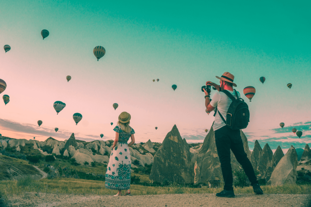 A man photographing dozens of hot air balloons in a picturesque mountain scenery.